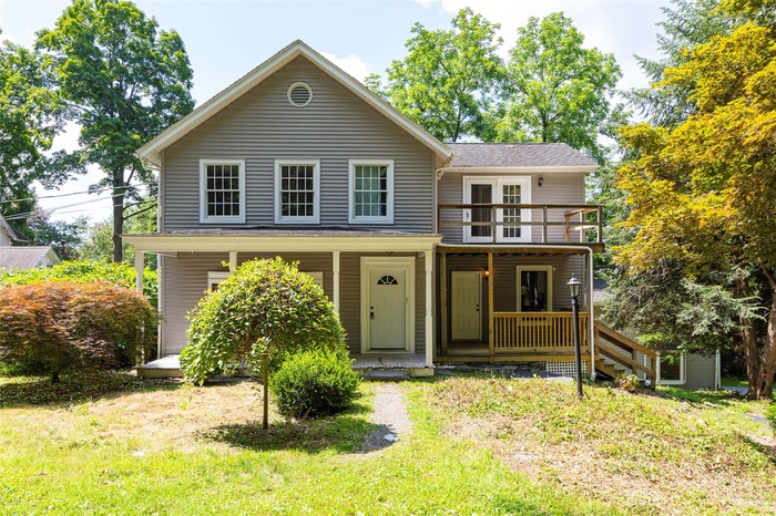 View of front of property featuring a balcony, a porch, a front lawn, and a shingled roof