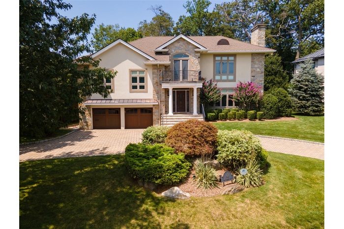 View of front of house featuring stone siding, a balcony, stucco siding, a garage, and a front lawn