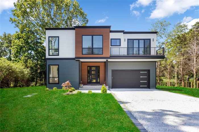 Modern home featuring a balcony, gravel driveway, a front lawn, and an attached garage