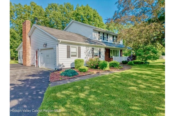 Traditional home with an attached garage, a chimney, asphalt driveway, and a front yard