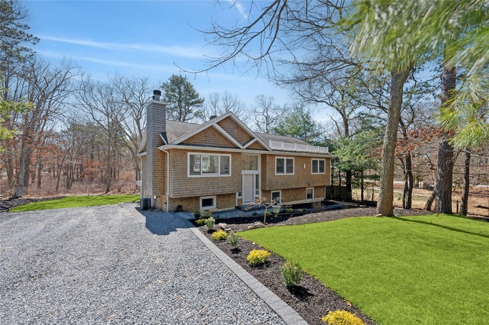 Bi-level home with gravel driveway, a front yard, roof mounted solar panels, central AC unit, and a chimney