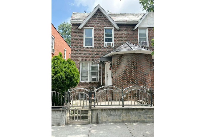 Traditional-style home with a fenced front yard, brick siding, a gate, and a high end roof