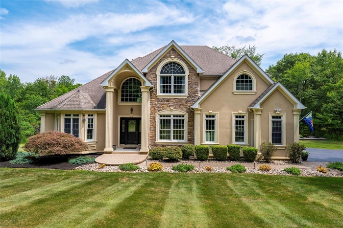 View of front of property featuring stucco siding, stone siding, a front yard, and roof with shingles
