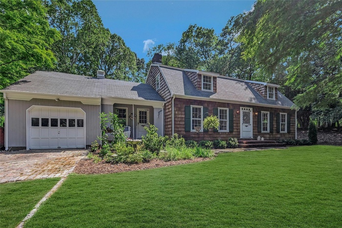 View of front of house with a chimney, a garage, roof with shingles, and a front yard