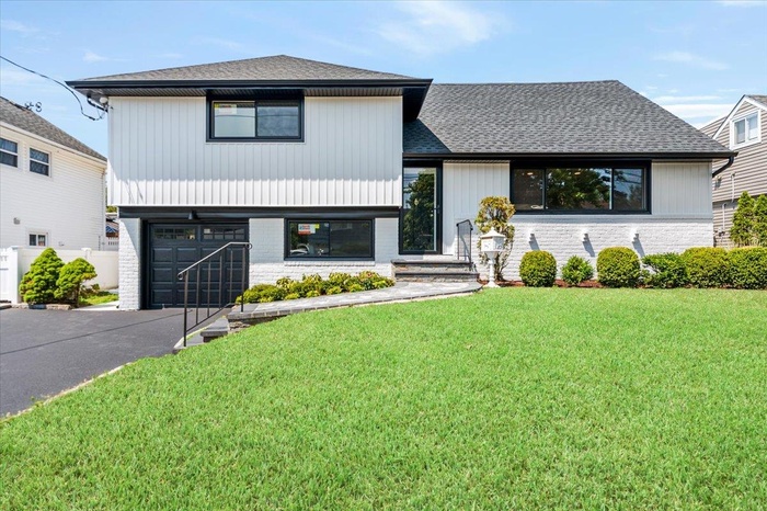Split level home featuring driveway, a front yard, a shingled roof, an attached garage, and brick siding