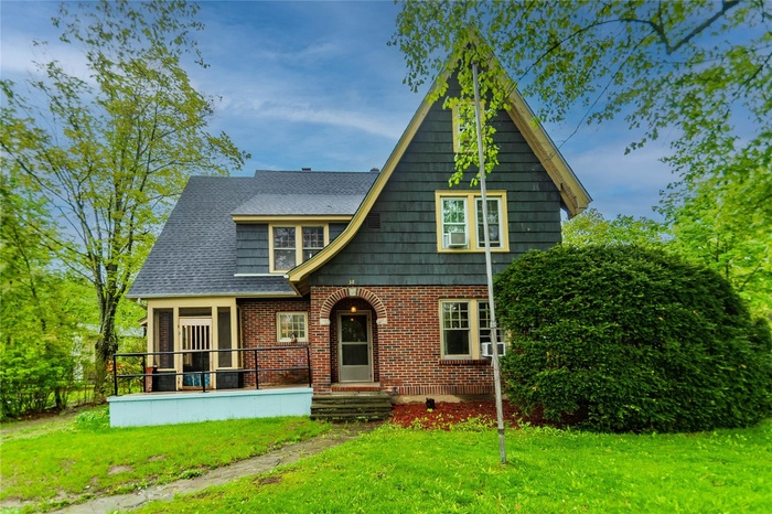 English style home with a front lawn, brick siding, and cooling unit