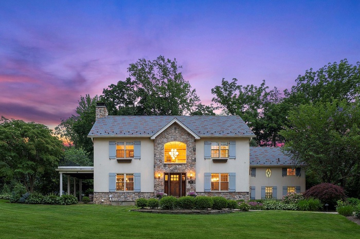 View of front of property featuring stone siding, a chimney, stucco siding, and a high end roof