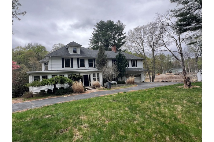 View of front of property with a front yard, driveway, an attached garage, and a chimney