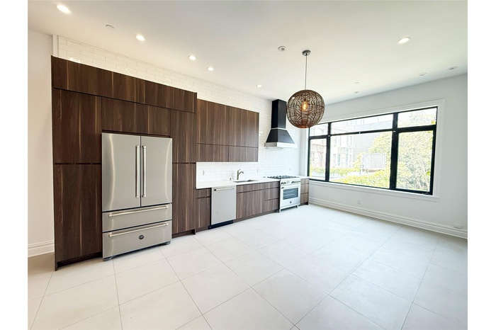 Kitchen featuring high quality appliances, modern cabinets, custom exhaust hood, light countertops, and decorative backsplash