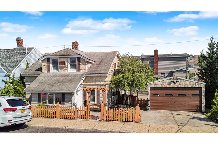 View of front of house featuring a fenced front yard, a garage, roof with shingles, and an outdoor structure