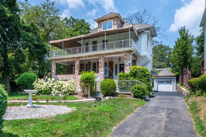 View of front of home featuring a balcony, stone siding,  driveway, garage and covered porch