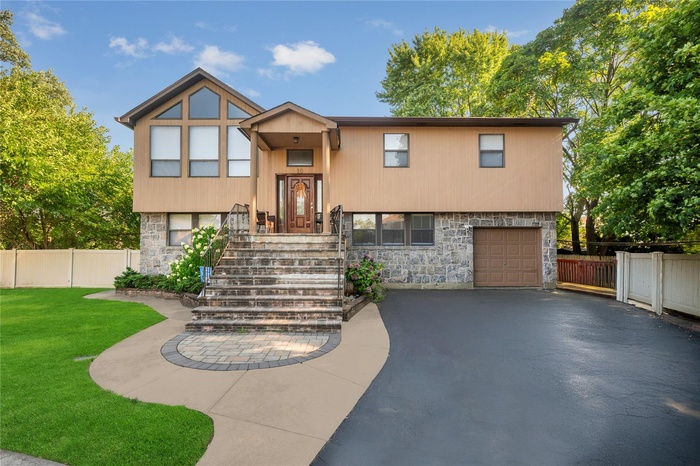 Bi-level home featuring stone siding, an attached garage, and asphalt driveway