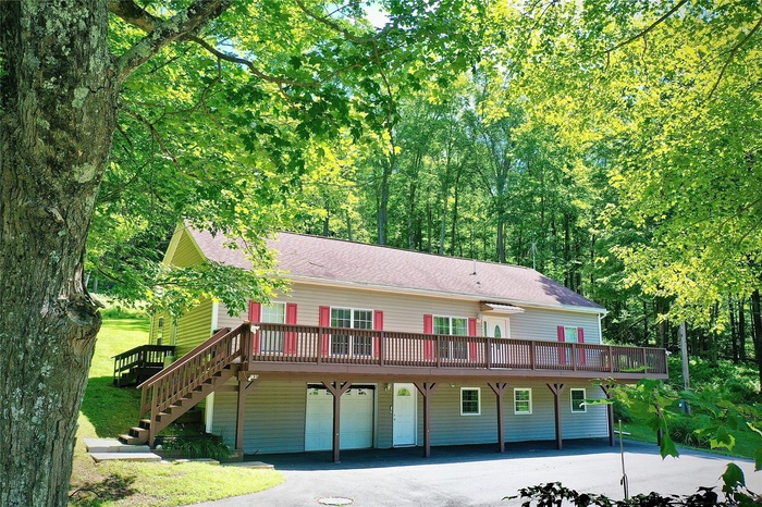 View of front facade featuring a wooden deck, a garage, asphalt driveway, a shingled roof, and stairs
