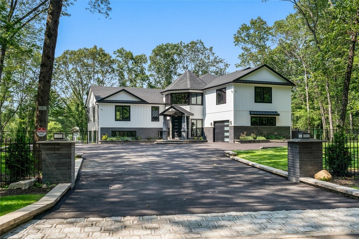 Modern farmhouse featuring driveway, a shingled roof, and brick siding