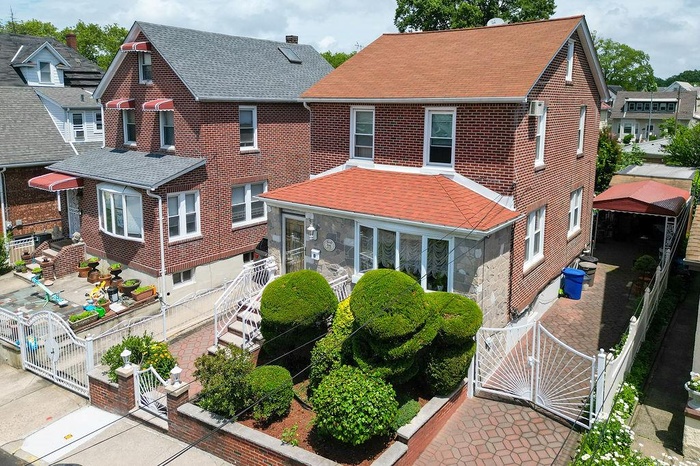 View of front facade featuring a gate, brick siding, a shingled roof, and a sunroom