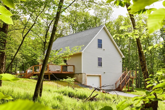 View of side of home featuring stairs, a shingled roof, an attached garage, and a deck