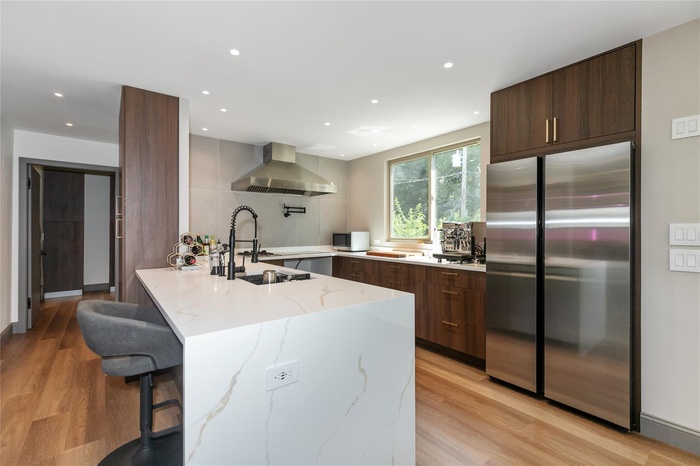 Kitchen with modern cabinets, appliances with stainless steel finishes, a peninsula, wall chimney exhaust hood, and a kitchen breakfast bar