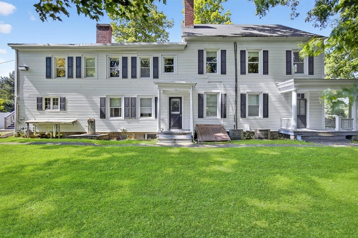 Rear view of house featuring a chimney and a lawn