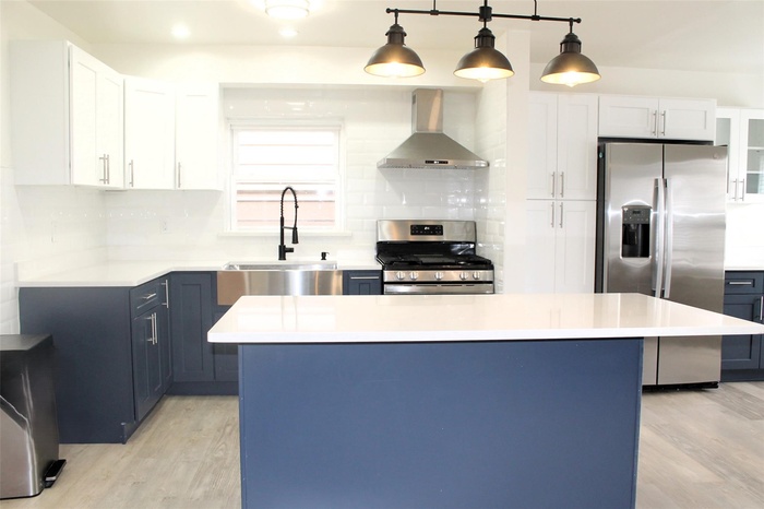 Kitchen with light wood finished floors, tasteful backsplash, appliances with stainless steel finishes, and wall chimney range hood