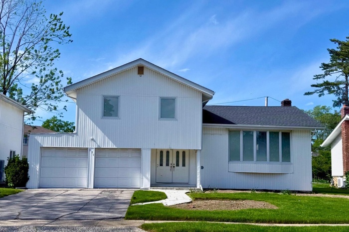Tri-level home with an attached garage, driveway, a chimney, a front lawn, and a shingled roof