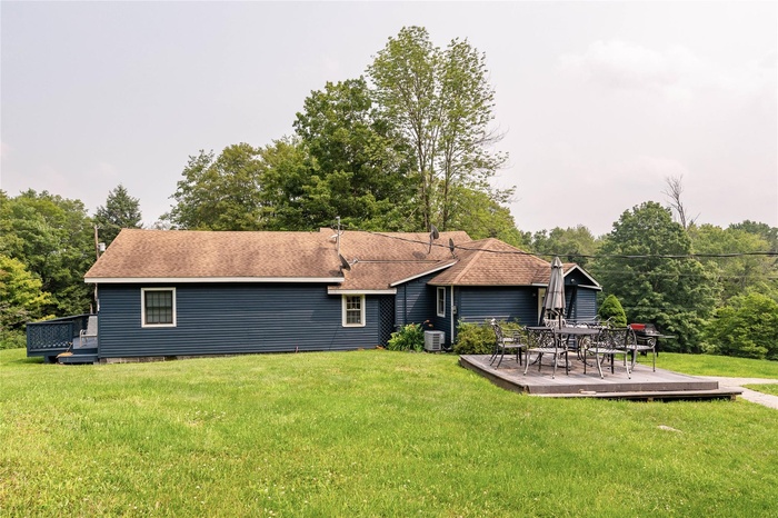 Back of property featuring a deck, a lawn, and roof with shingles