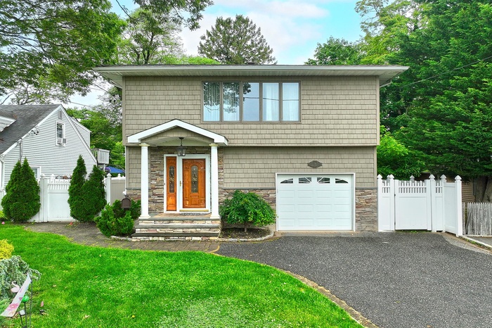 View of front facade featuring stone siding, a garage, and driveway