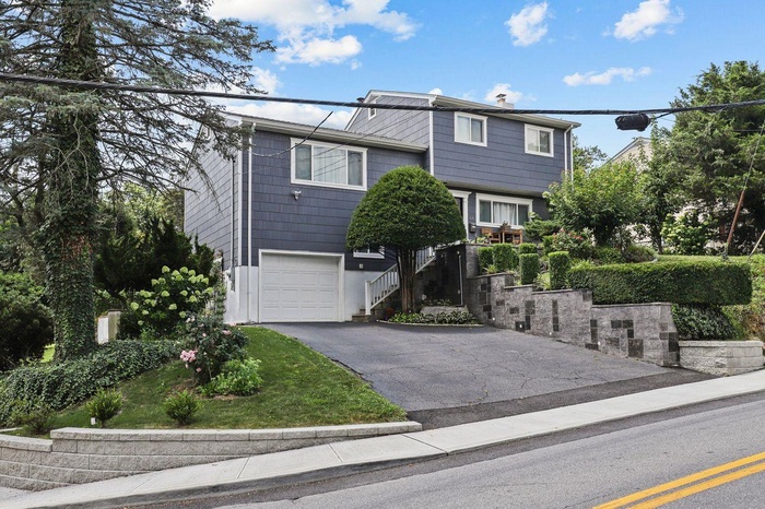 View of front of home featuring driveway, a garage, a chimney, and stairs