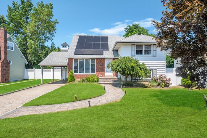 View of front of house featuring roof with shingles, concrete driveway, an attached carport, roof mounted solar panels, and brick siding