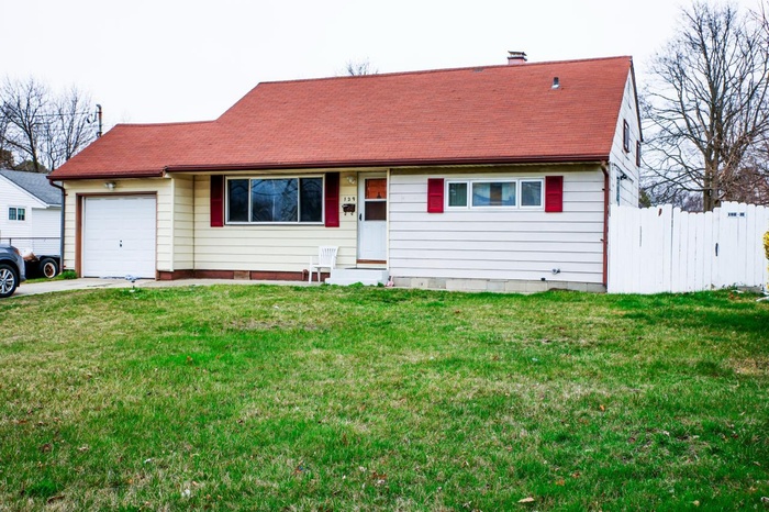 View of front of house featuring an attached garage, fence, a front lawn, and roof with shingles