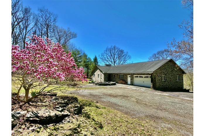 View of front facade with a chimney, a garage, driveway, and stone siding