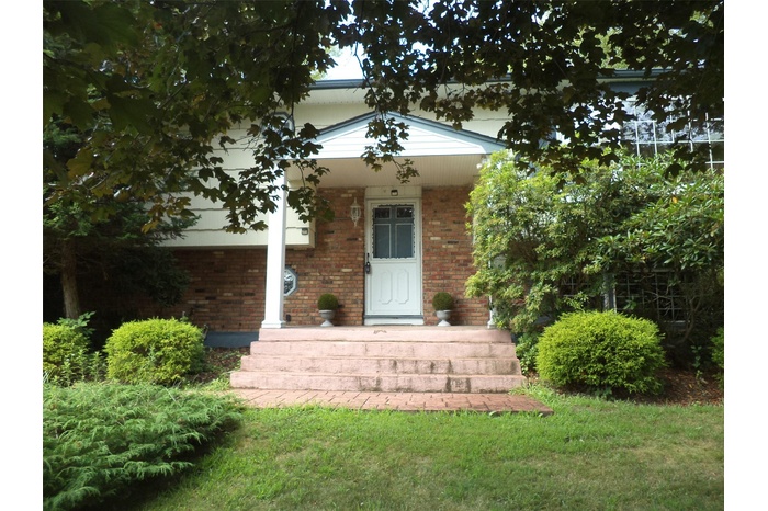 View of exterior entry with brick siding, covered porch, and a yard