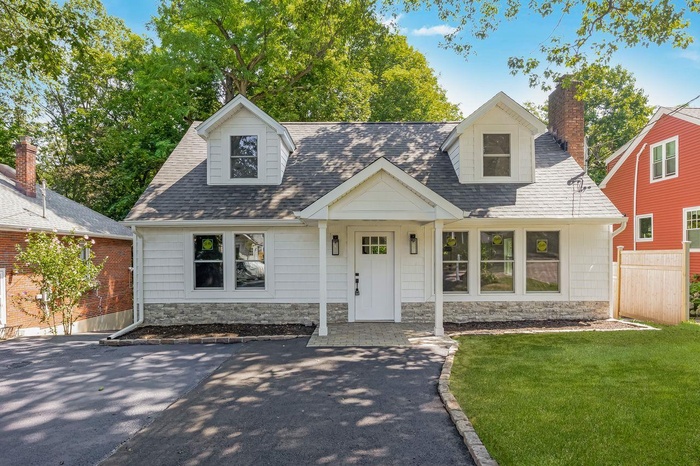 Cape cod home with stone siding, a shingled roof, and a chimney