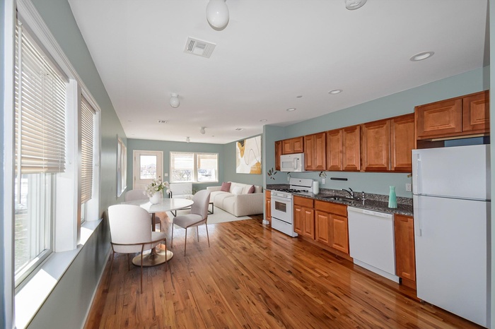 Kitchen and living room featuring white appliances, wood finished floors, brown cabinetry, open floor plan, and dark stone countertops