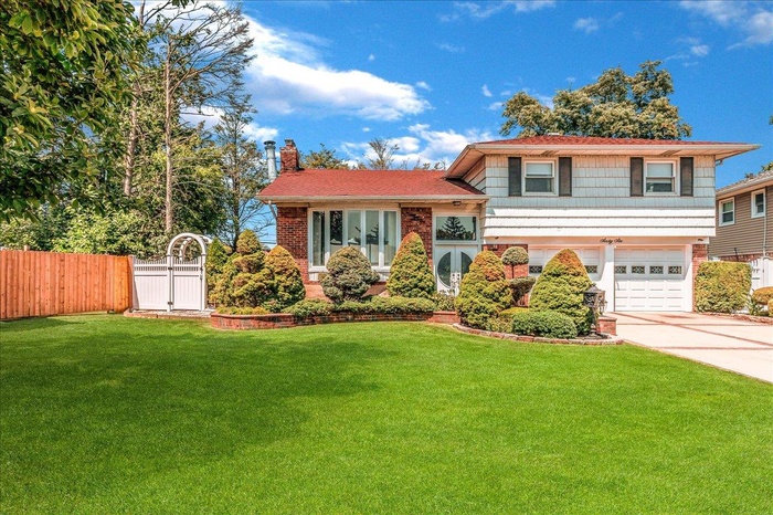Split level home with brick siding, a chimney, driveway, an attached garage, and a gate