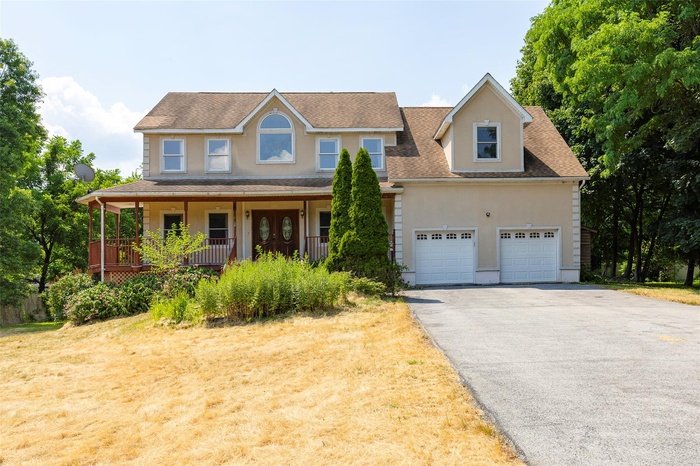 View of front facade with roof with shingles, covered porch, asphalt driveway, and a front yard