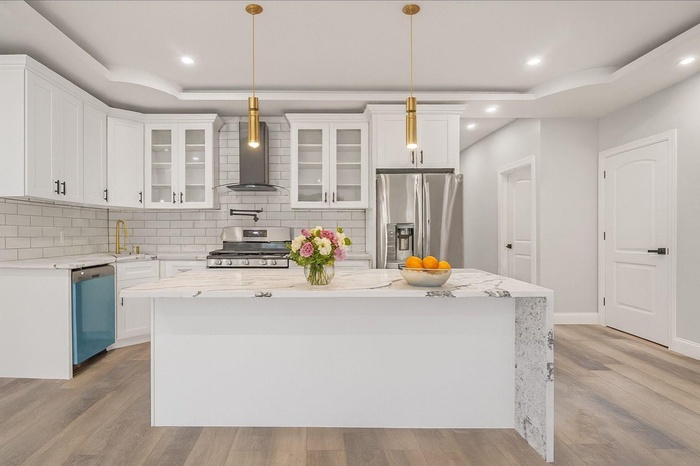 Kitchen featuring a tray ceiling, appliances with stainless steel finishes, a center island, wall chimney range hood, and recessed lighting