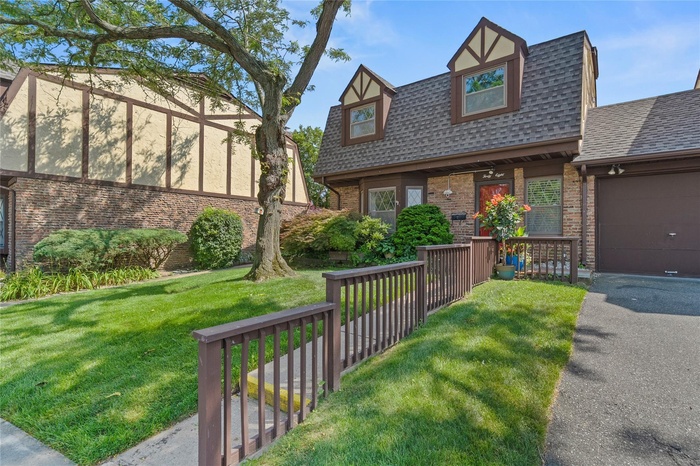 Tudor-style house featuring roof with shingles, brick siding, and a front lawn