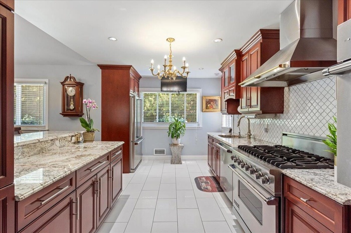 Kitchen with wall chimney range hood, high quality appliances, a chandelier, light tile patterned flooring, and tasteful backsplash