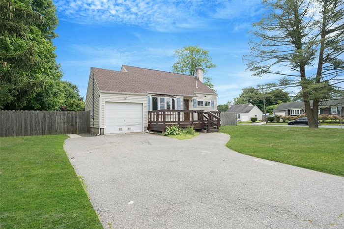 View of front facade featuring a garage, roof with shingles, a wooden deck, driveway, and a chimney