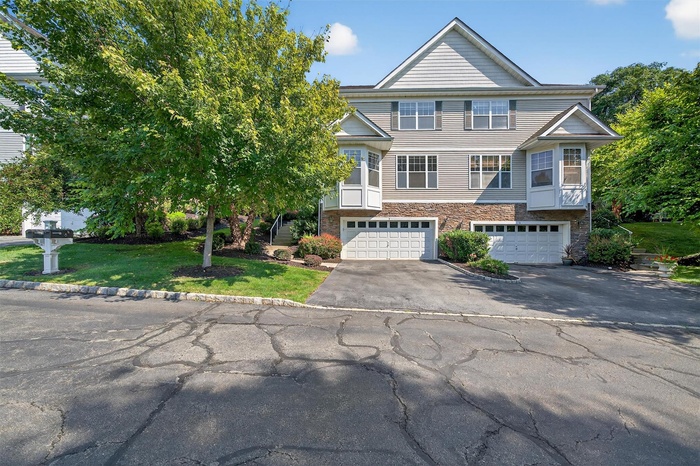 View of front of property with asphalt driveway, stone siding, a garage, and a front lawn