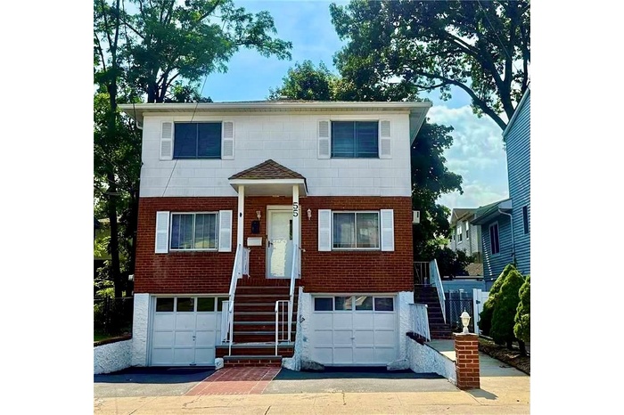 View of front facade with brick siding, driveway, an attached garage, and stairway