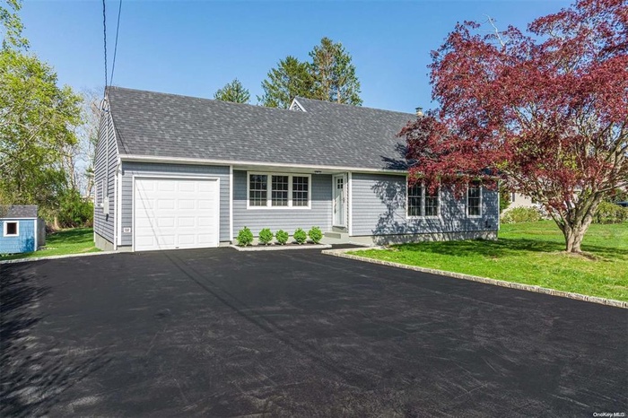 View of front facade with roof with shingles, a garage, asphalt driveway, and a front lawn