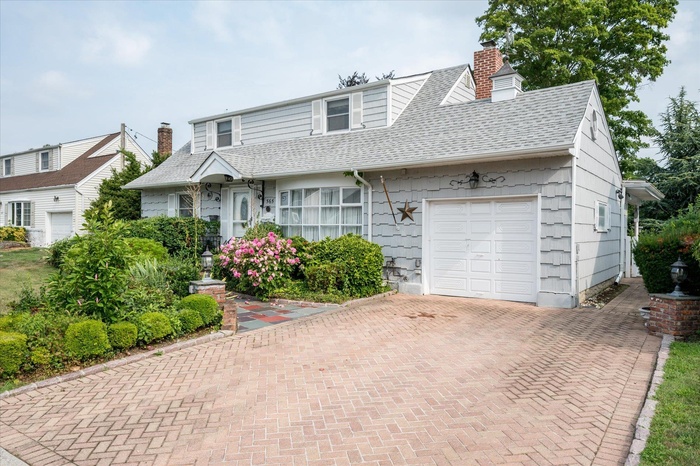 View of front facade featuring a garage, roof with shingles, a chimney, and decorative driveway