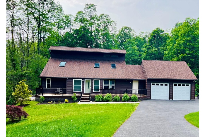 View of front of house with an attached garage, a porch, a front lawn, and a shingled roof