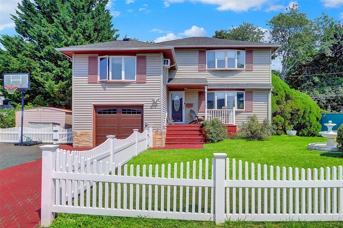 Split level home with a fenced front yard, an attached garage, roof with shingles, a porch, and stone siding