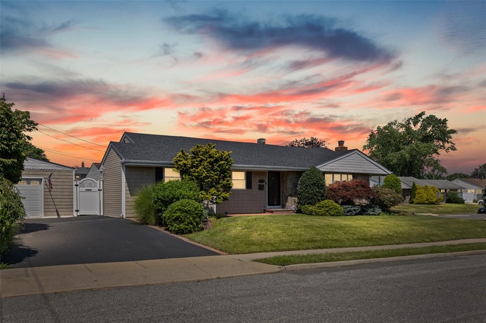 Ranch-style home featuring a gate, a chimney, a front lawn, a shingled roof, and a garage