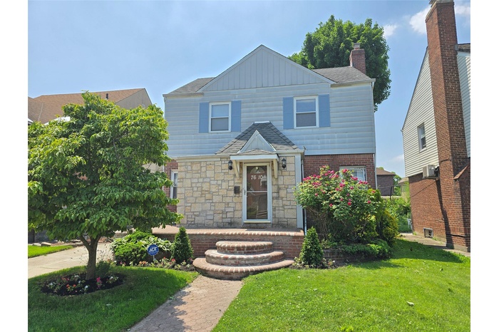 Traditional home featuring a front lawn, brick siding, cooling unit, board and batten siding, and stone siding