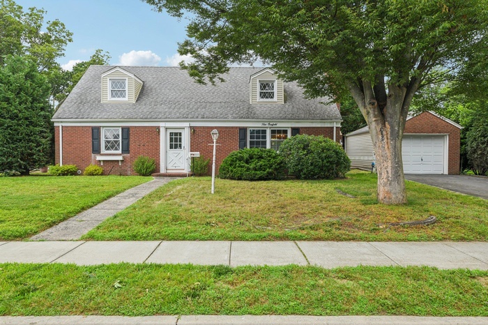 New england style home with brick siding, an outdoor structure, a garage, a front lawn, and driveway