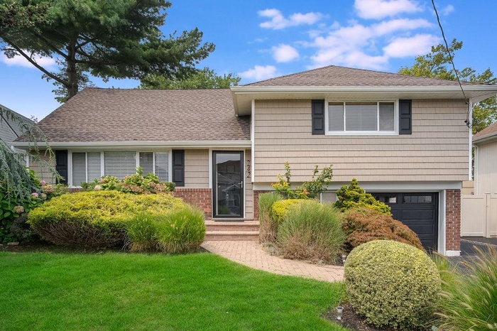 Split level home with roof with shingles, an attached garage, a front yard, and brick siding
