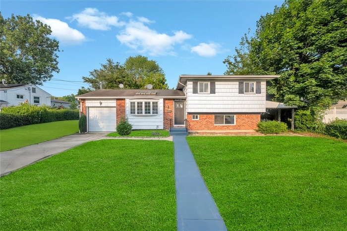 Tri-level home with brick siding, a front lawn, an attached garage, and driveway